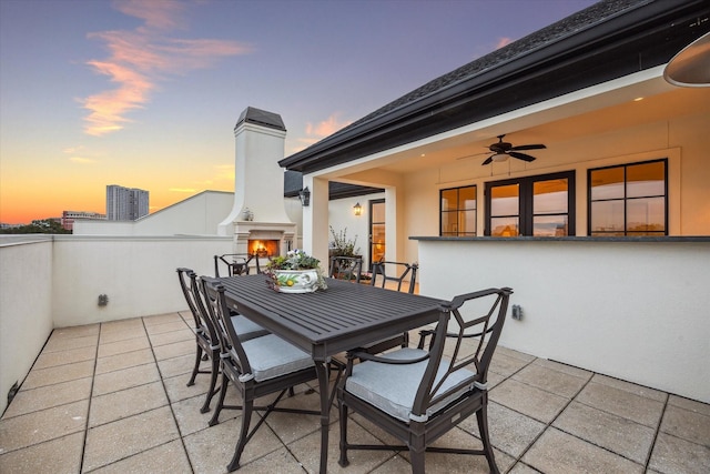 patio terrace at dusk featuring exterior fireplace and ceiling fan