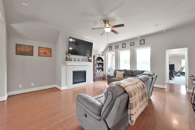 living room featuring a brick fireplace, built in shelves, light hardwood / wood-style floors, and ceiling fan