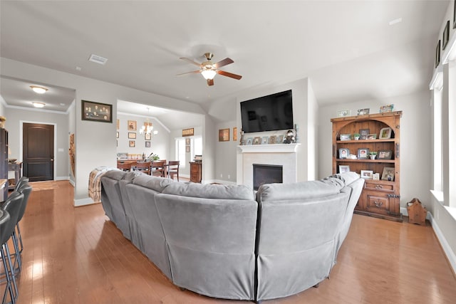 living room with ceiling fan with notable chandelier, light hardwood / wood-style floors, and vaulted ceiling