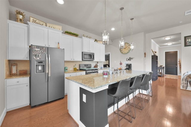 kitchen with decorative backsplash, appliances with stainless steel finishes, white cabinetry, and a center island with sink