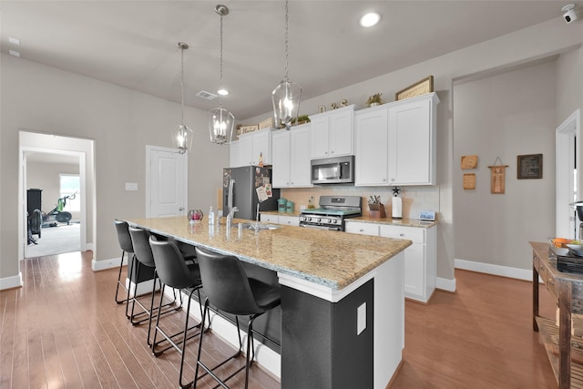 kitchen featuring white cabinetry, a center island with sink, appliances with stainless steel finishes, tasteful backsplash, and decorative light fixtures