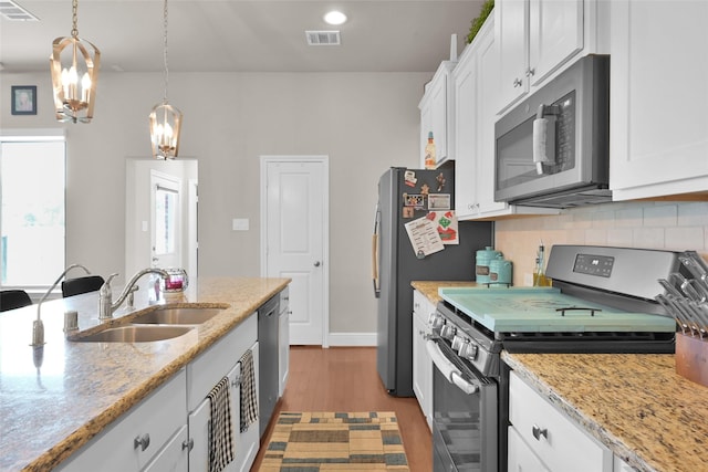 kitchen featuring pendant lighting, sink, stainless steel appliances, white cabinets, and light stone counters