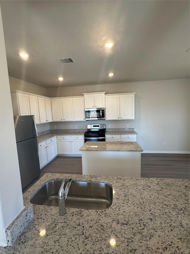 kitchen with a center island, sink, stainless steel appliances, white cabinets, and light stone counters