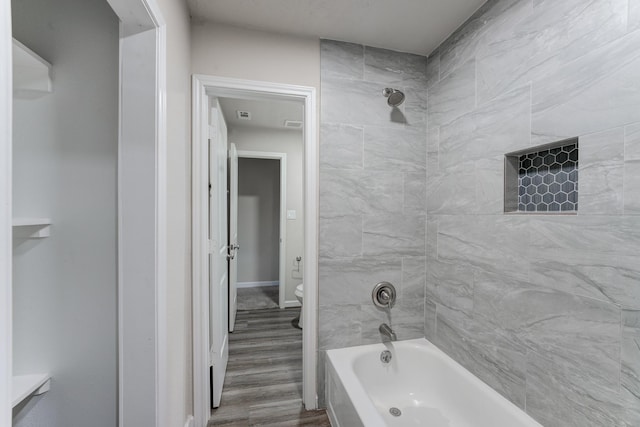 bathroom featuring hardwood / wood-style flooring, toilet, and tiled shower / bath