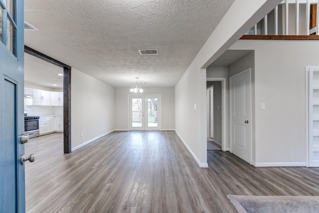 empty room with a textured ceiling, a chandelier, and light hardwood / wood-style flooring