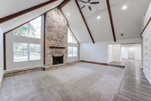 unfurnished living room featuring high vaulted ceiling, beam ceiling, ceiling fan, and a stone fireplace