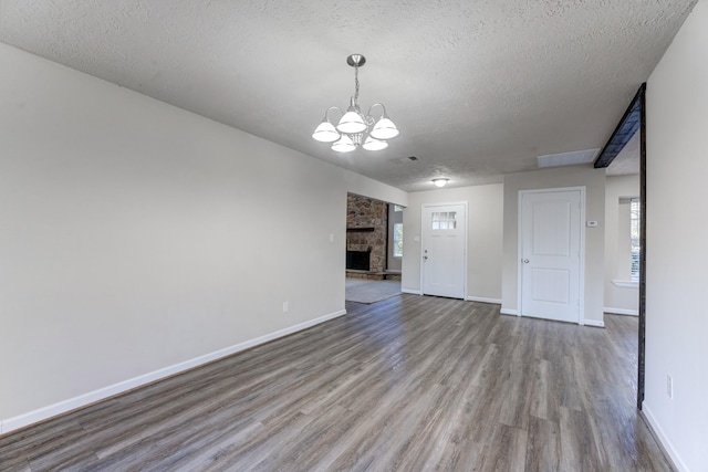 unfurnished living room with a textured ceiling, an inviting chandelier, hardwood / wood-style flooring, and a stone fireplace