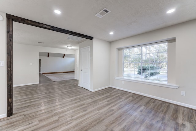 empty room featuring a textured ceiling, beam ceiling, and light hardwood / wood-style floors