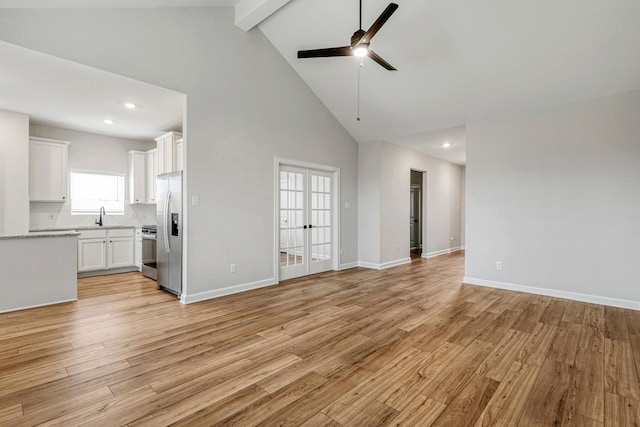 unfurnished living room featuring ceiling fan, light wood-type flooring, high vaulted ceiling, beam ceiling, and sink