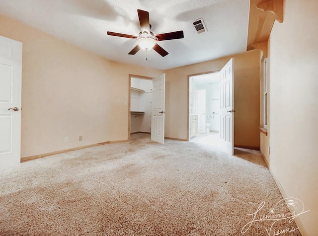 unfurnished bedroom with ceiling fan, light colored carpet, connected bathroom, a walk in closet, and a closet