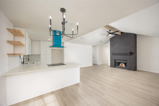 kitchen with a brick fireplace, kitchen peninsula, sink, white cabinetry, and a textured ceiling