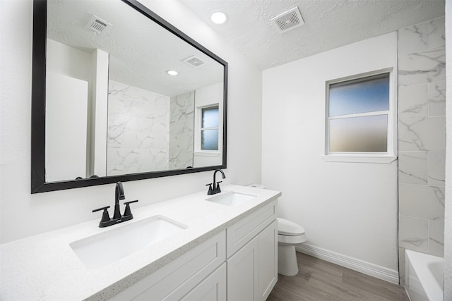 full bathroom with a textured ceiling, tiled shower / bath combo, hardwood / wood-style floors, vanity, and toilet