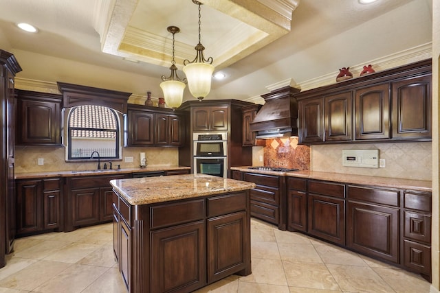 kitchen with pendant lighting, custom exhaust hood, sink, a tray ceiling, and a center island