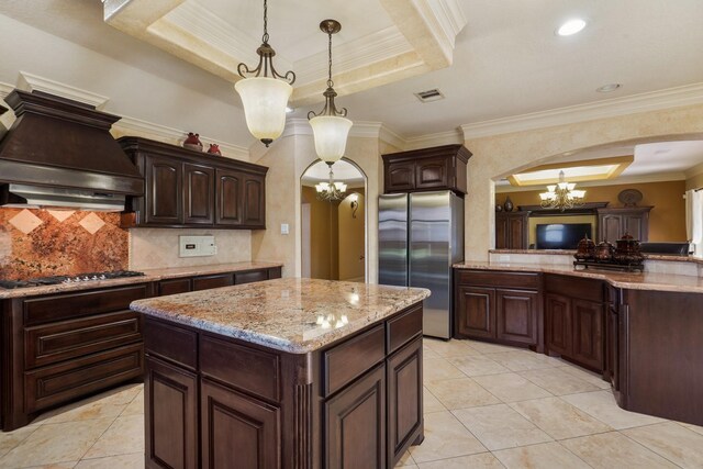 kitchen featuring a kitchen island, stainless steel appliances, an inviting chandelier, hanging light fixtures, and a tray ceiling