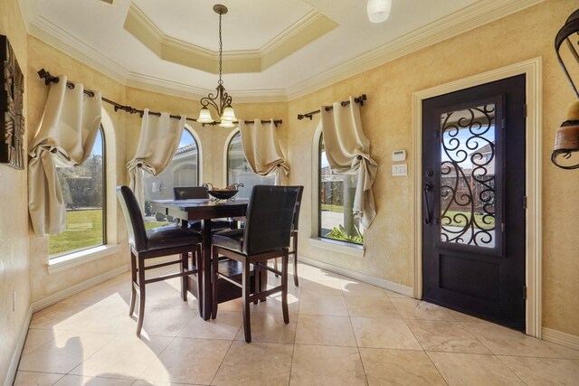 tiled dining room with ornamental molding, an inviting chandelier, and a tray ceiling