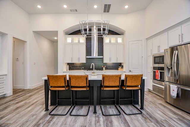 kitchen with white cabinets, appliances with stainless steel finishes, a center island with sink, and wall chimney exhaust hood