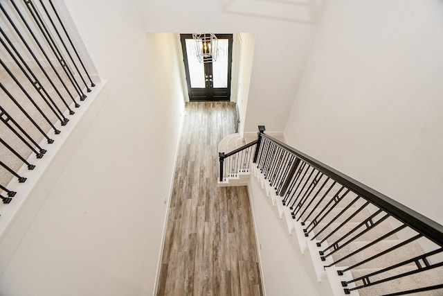 stairs with french doors, a chandelier, and hardwood / wood-style floors