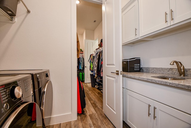 clothes washing area with cabinets, washer and clothes dryer, light hardwood / wood-style flooring, and sink