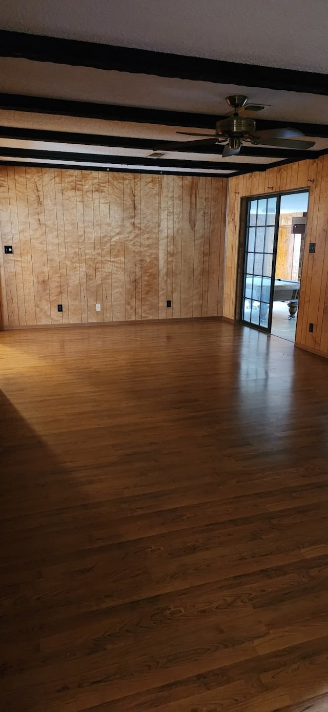 interior space with beamed ceiling, dark wood finished floors, a ceiling fan, and wooden walls