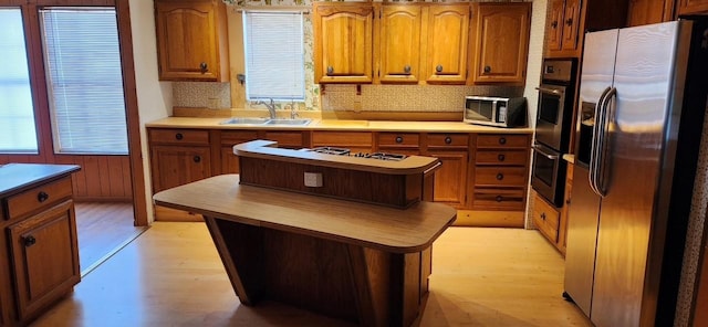 kitchen with brown cabinets, stainless steel appliances, a sink, and a center island