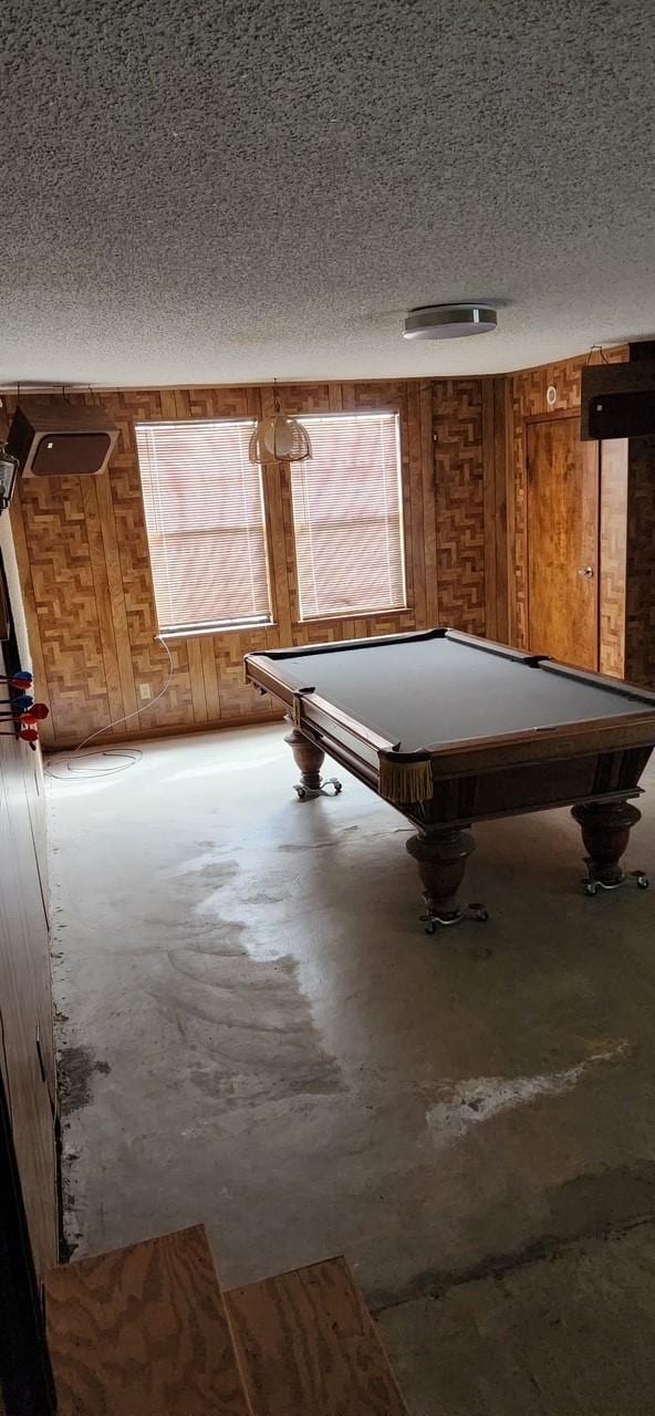 playroom with a textured ceiling, wood walls, concrete floors, and billiards