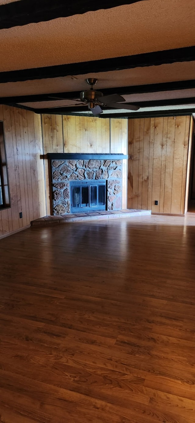 unfurnished living room with beam ceiling, ceiling fan, a stone fireplace, and wood finished floors