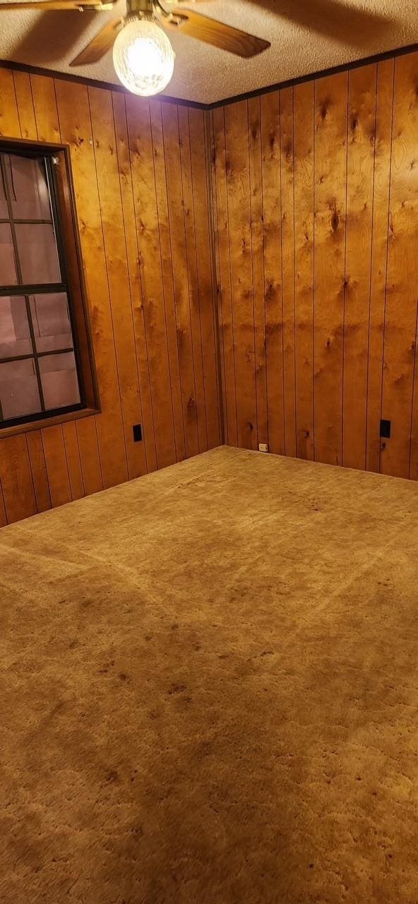 carpeted empty room featuring a textured ceiling, wood walls, and a ceiling fan