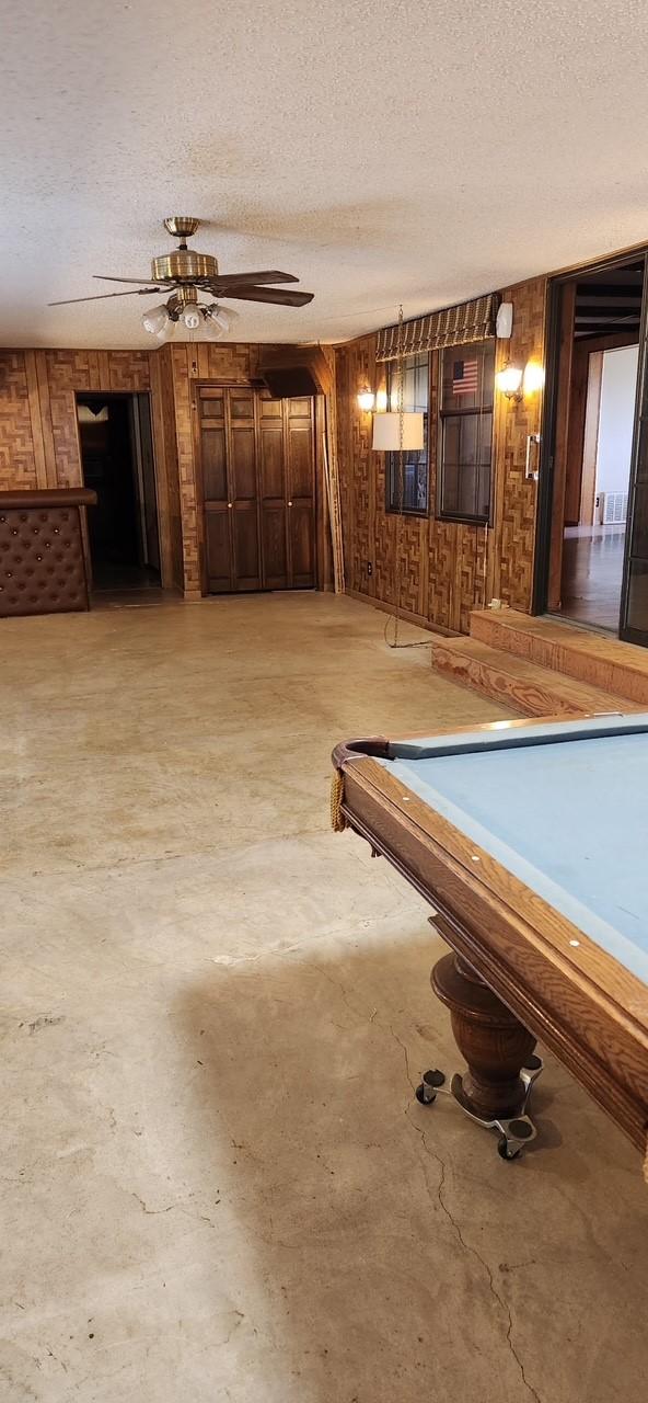 rec room featuring wood walls, ceiling fan, concrete flooring, and a textured ceiling