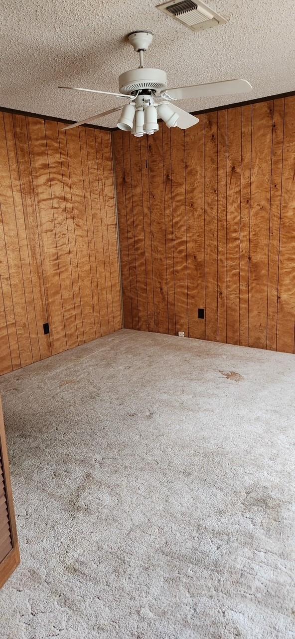 carpeted spare room with wooden walls, visible vents, and a textured ceiling