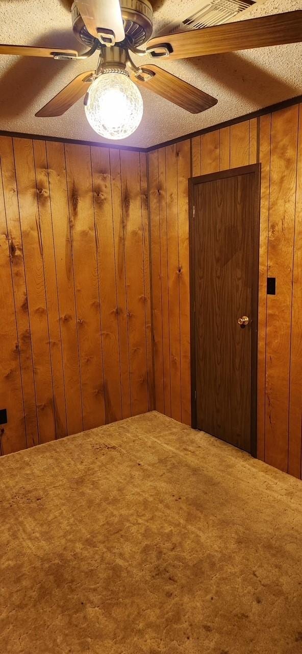 interior space with wood walls, a textured ceiling, and ceiling fan