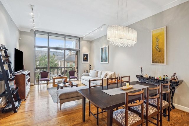 dining room with light wood-type flooring, an inviting chandelier, rail lighting, and expansive windows