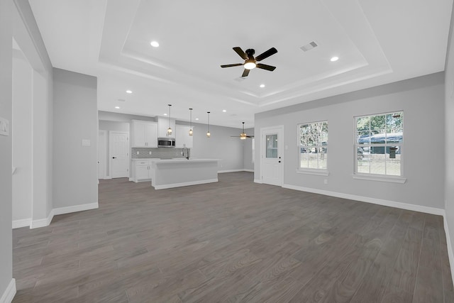 unfurnished living room with a raised ceiling, ceiling fan, sink, and hardwood / wood-style floors