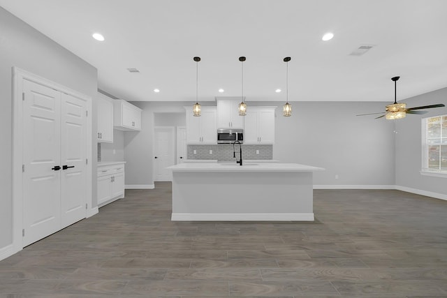 kitchen with ceiling fan, backsplash, sink, an island with sink, and white cabinets