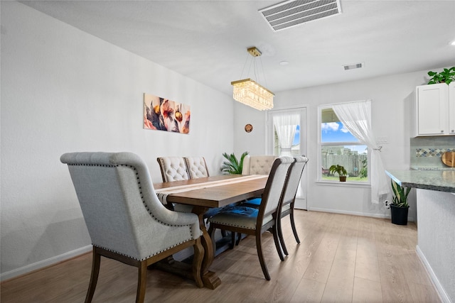 dining space with light hardwood / wood-style floors and a notable chandelier