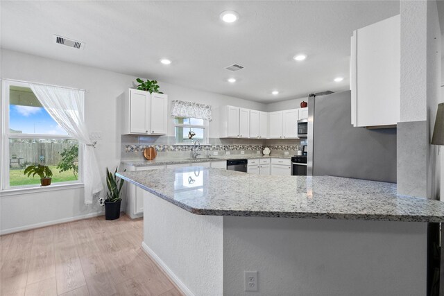 kitchen with kitchen peninsula, backsplash, light stone counters, and white cabinetry