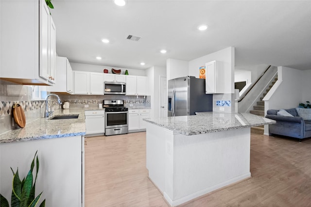 kitchen featuring kitchen peninsula, sink, white cabinetry, appliances with stainless steel finishes, and light stone counters