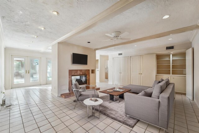 living room featuring a textured ceiling, crown molding, a tiled fireplace, and built in shelves