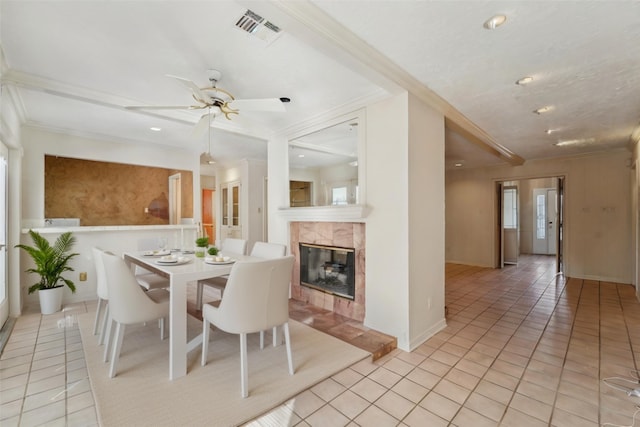 dining area featuring a tile fireplace, visible vents, crown molding, and light tile patterned flooring