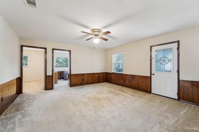 interior space featuring ceiling fan, plenty of natural light, light carpet, and wooden walls