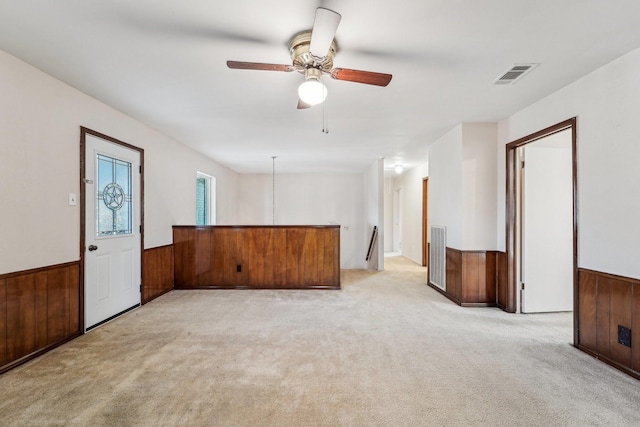 empty room featuring light colored carpet, wainscoting, visible vents, and wood walls