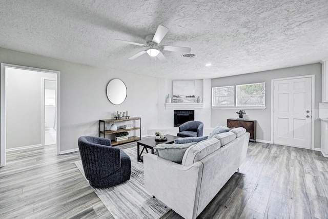 living room with ceiling fan, light wood-type flooring, a large fireplace, and a textured ceiling