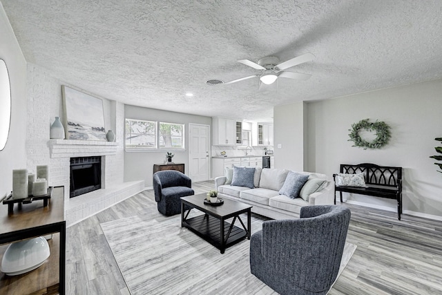 living room with light hardwood / wood-style floors, ceiling fan, a fireplace, a textured ceiling, and sink