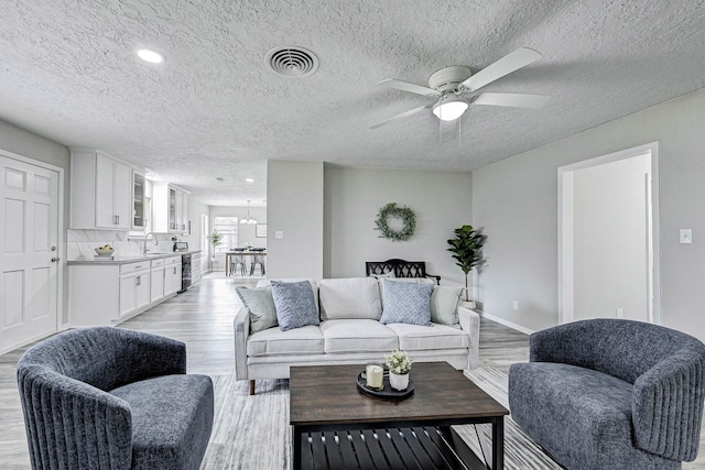 living room with ceiling fan, sink, a textured ceiling, and light hardwood / wood-style floors