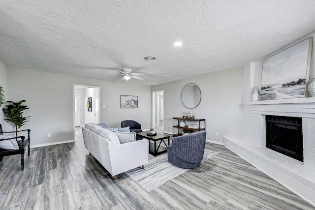 living room with ceiling fan, a textured ceiling, hardwood / wood-style floors, and a fireplace