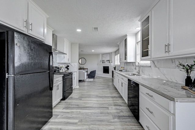 kitchen with black appliances, decorative backsplash, wall chimney exhaust hood, and white cabinetry