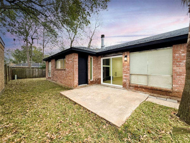 back house at dusk featuring a lawn and a patio area