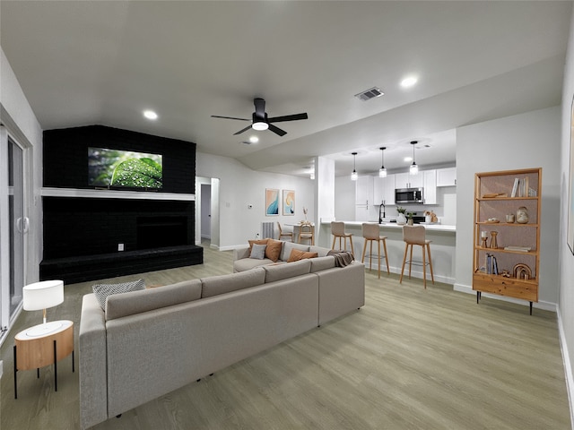 living room featuring vaulted ceiling, ceiling fan, light hardwood / wood-style flooring, and sink