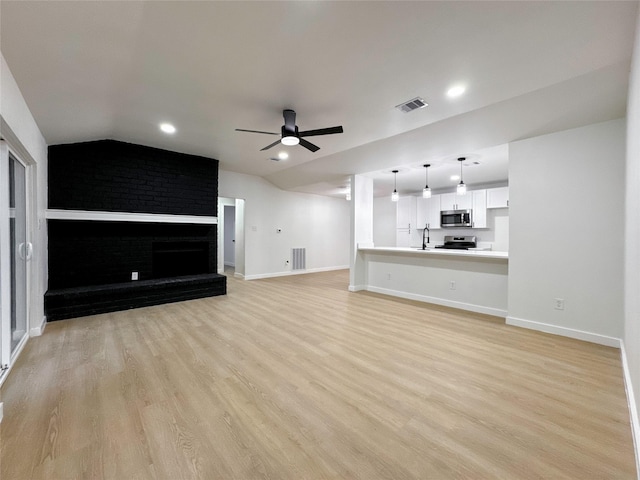 unfurnished living room with ceiling fan, a brick fireplace, light wood-type flooring, vaulted ceiling, and sink