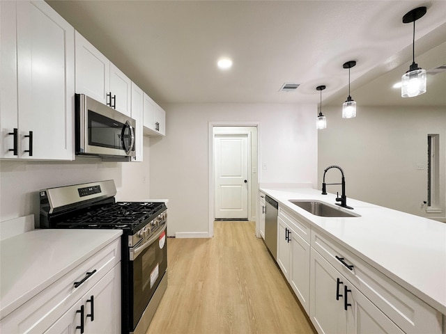 kitchen featuring light hardwood / wood-style floors, sink, white cabinetry, hanging light fixtures, and stainless steel appliances