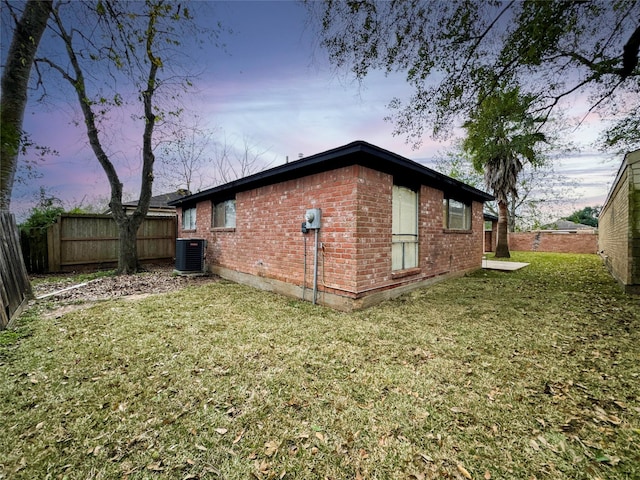 property exterior at dusk featuring a lawn and central AC unit